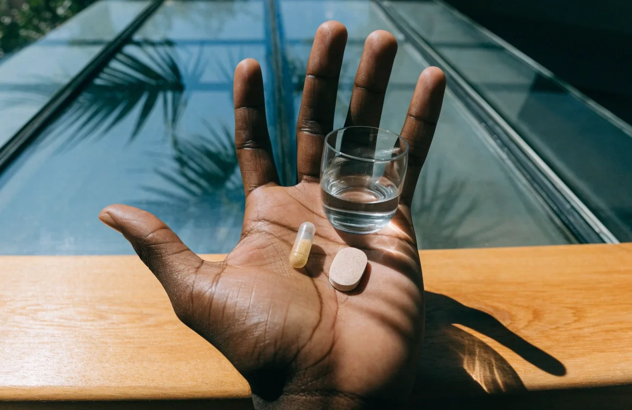 One translucent capsule on pale paper under hard noon light with a leaf shadow crossing the sheet